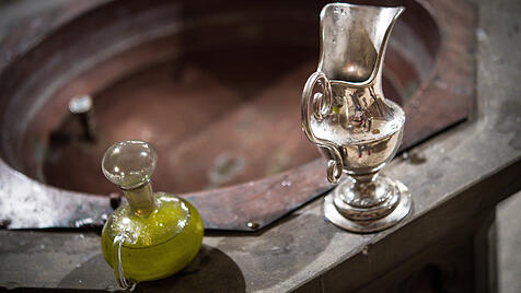 Eine Wasserkaraffe und Chrisamöl in einem Glasflakon stehen am Rande des Taufbeckens für eine Taufe bereit.