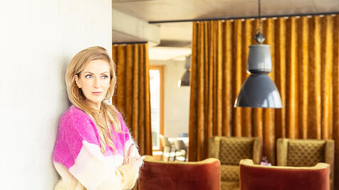 Dr. Katja Kessler vor einer Kombination aus Industrieleuchte und Vintage-Polstergarnitur.