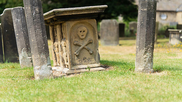 Ein alter Grabstein auf einem englischen Friedhof zeigt Schädel und Knochen als Symbole für den Tod.