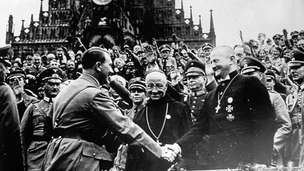 Adolf Hitler schüttelt die Hand des künftigen „Reichsbischofs“ Ludwig Müller, zwischen ihnen Abt Albanus Schachleiter (OSB).