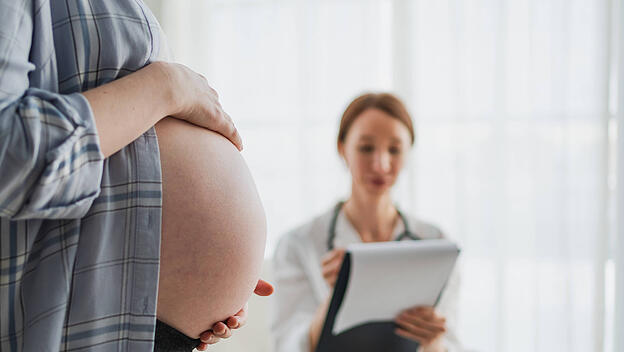 Schwangere Frau Hände berühren großen Bauch in Arztpraxis. Weiblicher Arzt untersucht schwangere Frau. Gynäkologe Arzt berät Patientin über Schwangerschaft im Krankenhaus. Besuch beim Arzt medizinischen Checkup.
