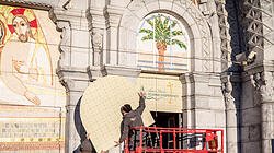 Arbeiter halten eine Abdeckung, die zur Verhüllung des Mosaiks am Eingang der Rosenkranz-Basilika angebracht wird, am 31. März 2025 in Lourdes (Frankreich). Das Mosaik ist ein Kunstwerk von Priester und Künstler Marko Ivan Rupnik, der unter Verdacht steht, sexuellen Missbrauch begangen zu haben.