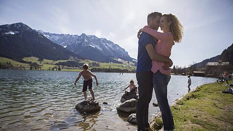 Austria Tyrol Walchsee happy couple embracing at the lake with family in background model release