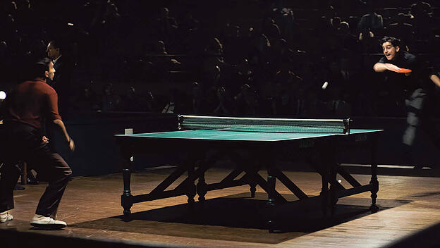 Timothée Chalamet (frontal) schmettert am grünen Tisch: eine Szene aus dem Film „Marty Supreme“.