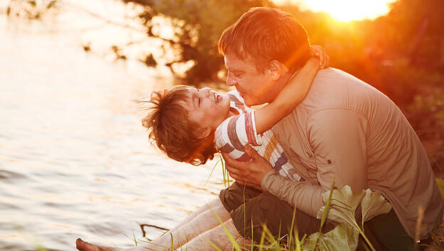 Glücklicher Vater und Sohn spielen bei Sonnenuntergang am Fluss.